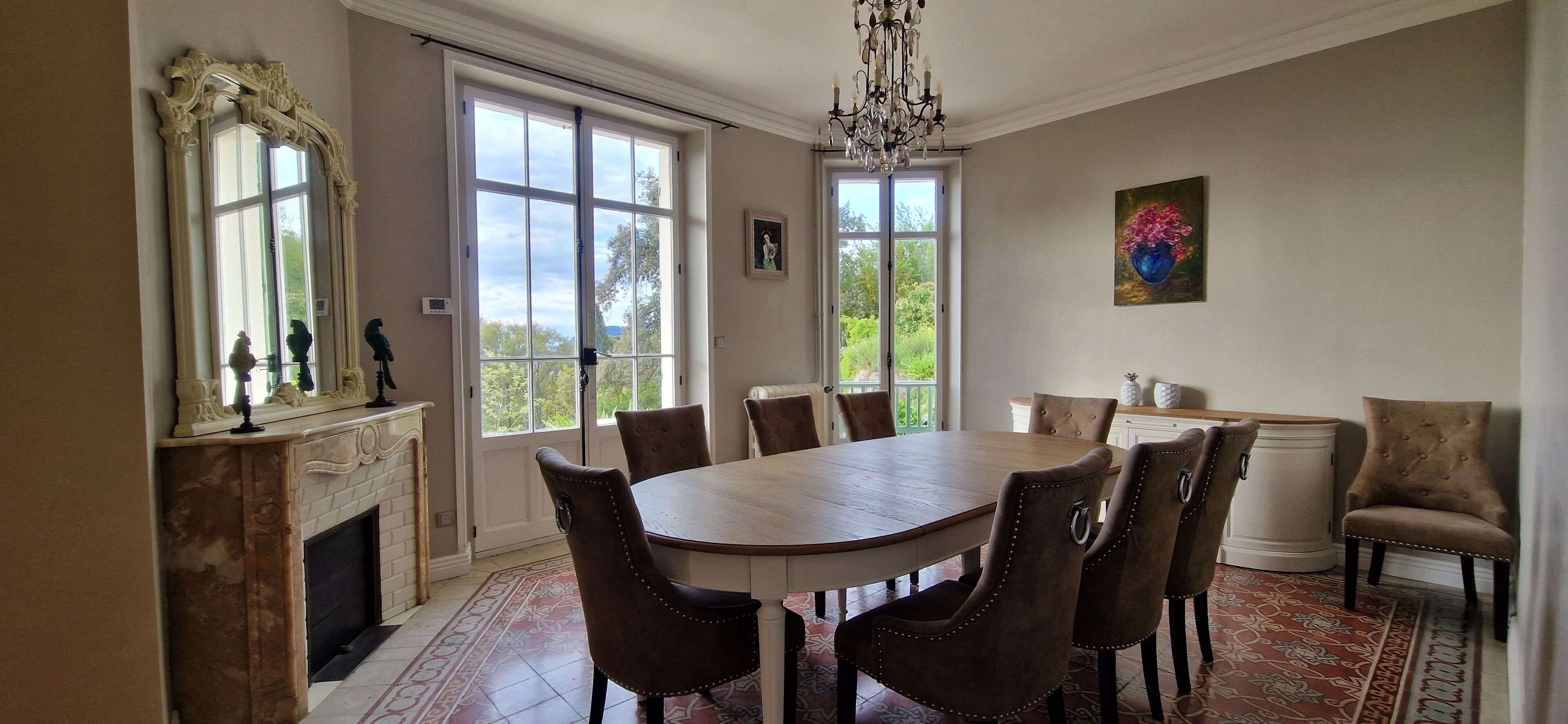 Une salle à manger avec une grande table en bois, huit chaises rembourrées, une cheminée et un lustre.