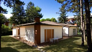 Ein eingeschossiges Haus mit Ziegeldach, einer kleinen Terrasse mit Tisch und Stühlen und einem gepflegten Rasen.