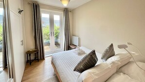 A bedroom with a bed, a bedside table, a lamp, and a view of the outside through a sliding door. - Modern Cosy home, Limeslade Bay - Pass the Keys (The Mumbles)