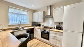 A modern kitchen with white cabinets, a built-in oven, a microwave, a toaster, and a refrigerator. - Modern Cosy home, Limeslade Bay - Pass the Keys (The Mumbles)