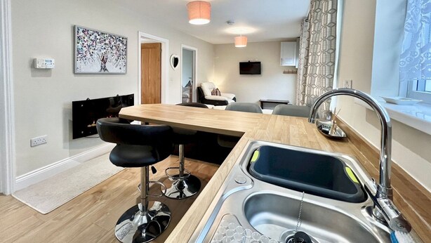 A modern kitchen with a central island, bar stools, a built-in sink, and a dining area. - Modern Cosy home, Limeslade Bay - Pass the Keys (The Mumbles)