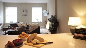 Ein Essbereich mit einem Tisch, der für das Frühstück gedeckt ist, mit Croissants, Käse und Erdbeeren. Über dem Tisch hängen zwei Pendelleuchten, und an der Seite steht eine Lampe.