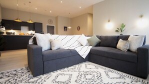 Ein modernes Wohnzimmer mit einem dunkelgrauen Moduls Sofa, einem gemusterten Teppich und Pendelleuchten.