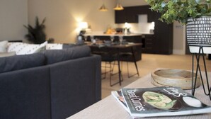 Ein modernes Wohnzimmer mit einem dunklen Sofa, einem Essbereich mit Holztisch und einer Küche im Hintergrund.
