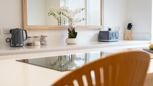 Eine moderne Küche mit weißer Arbeitsplatte, einer Kaffeemaschine, einem Toaster und einer Vase mit weißen Blumen.