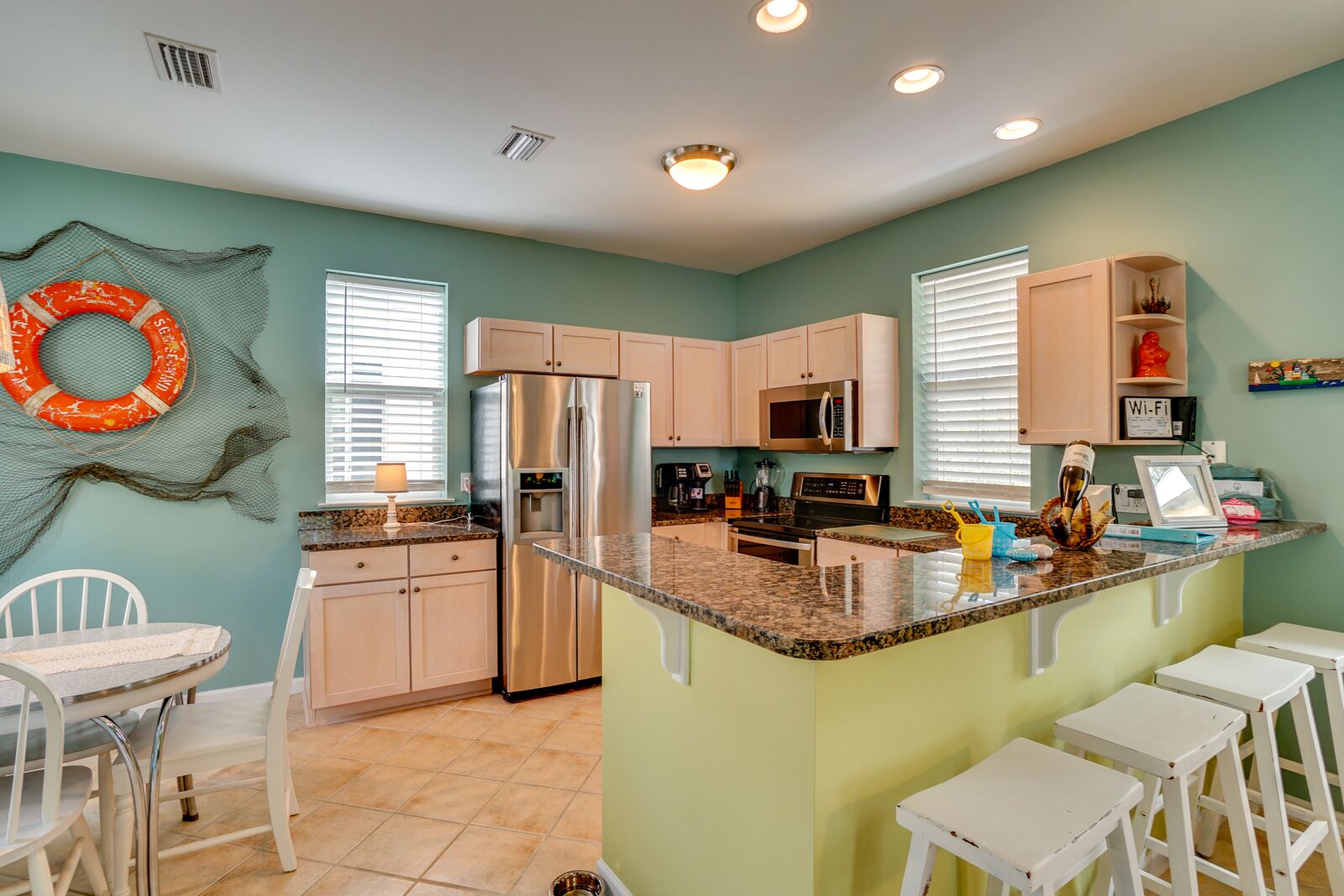 A modern kitchen with a central island, white bar stools, and a dining area with a white table and chairs.
