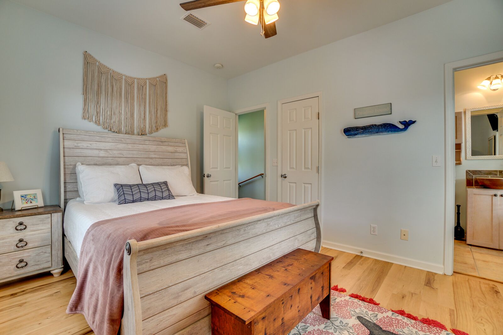 A bedroom with a wooden bed, a bench, a nightstand, and a wall-mounted macrame piece.