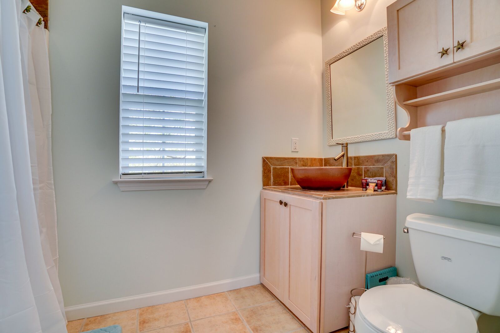 Une salle de bain avec des toilettes, un lavabo et une fenêtre équipée de stores.