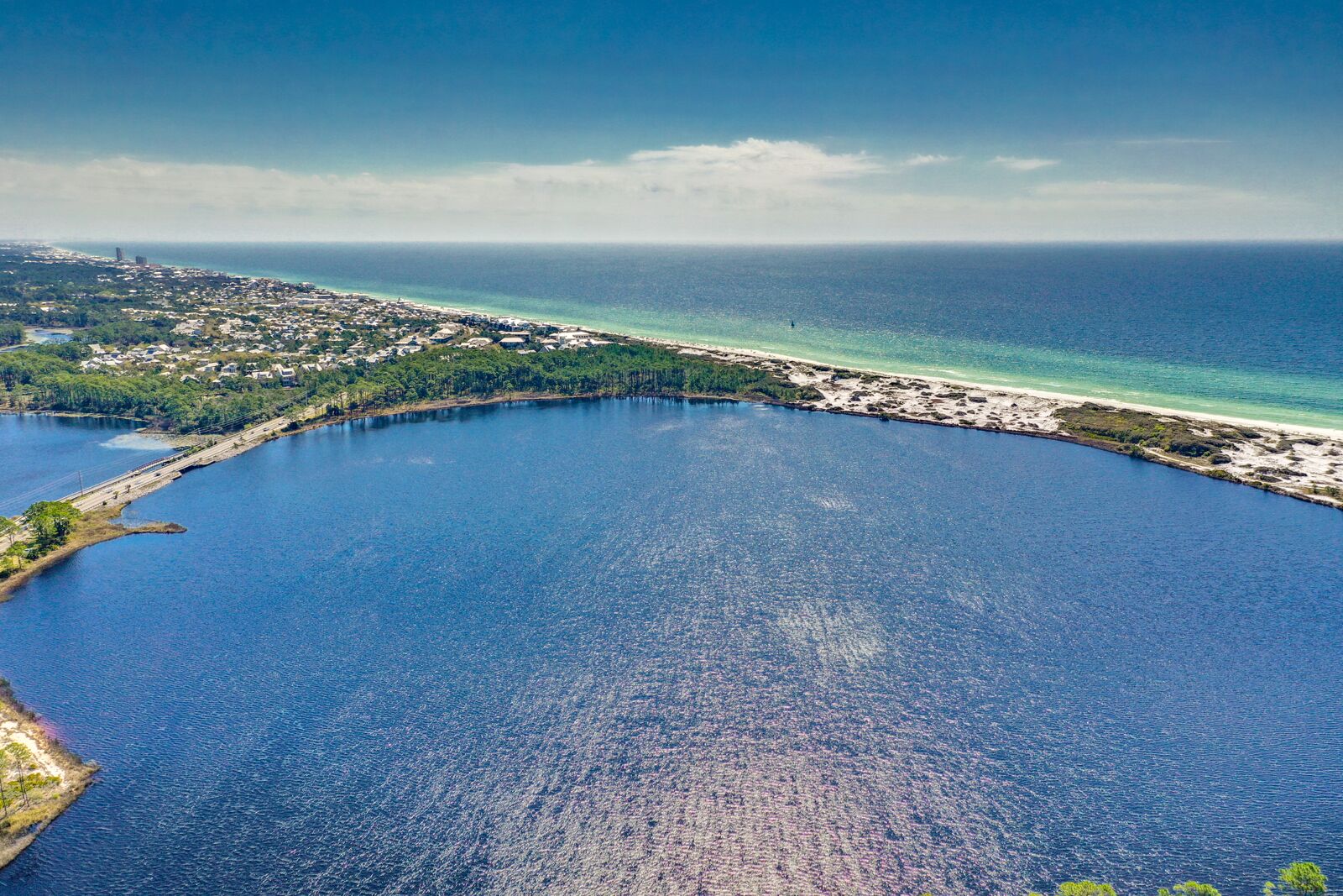 An aerial view of a coastal area with a large body of water, a beach, and a densely populated urban area in the background.