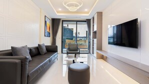 A modern living room with a sofa, ottoman, and a TV mounted on the wall. - Madison Saigon  By An Gia Hospitality (Ho Chi Minh City)