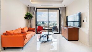 A modern living room with a sofa, a glass coffee table, a TV, and a view of the city through large windows. - Madison Saigon  By An Gia Hospitality (Ho Chi Minh City)