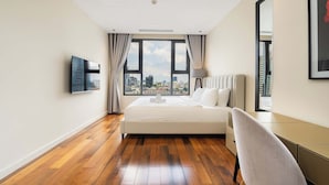 A hotel room with a large bed, a TV mounted on the wall, a view of the city through large windows, and a chair by the window. - Madison Saigon  By An Gia Hospitality (Ho Chi Minh City)
