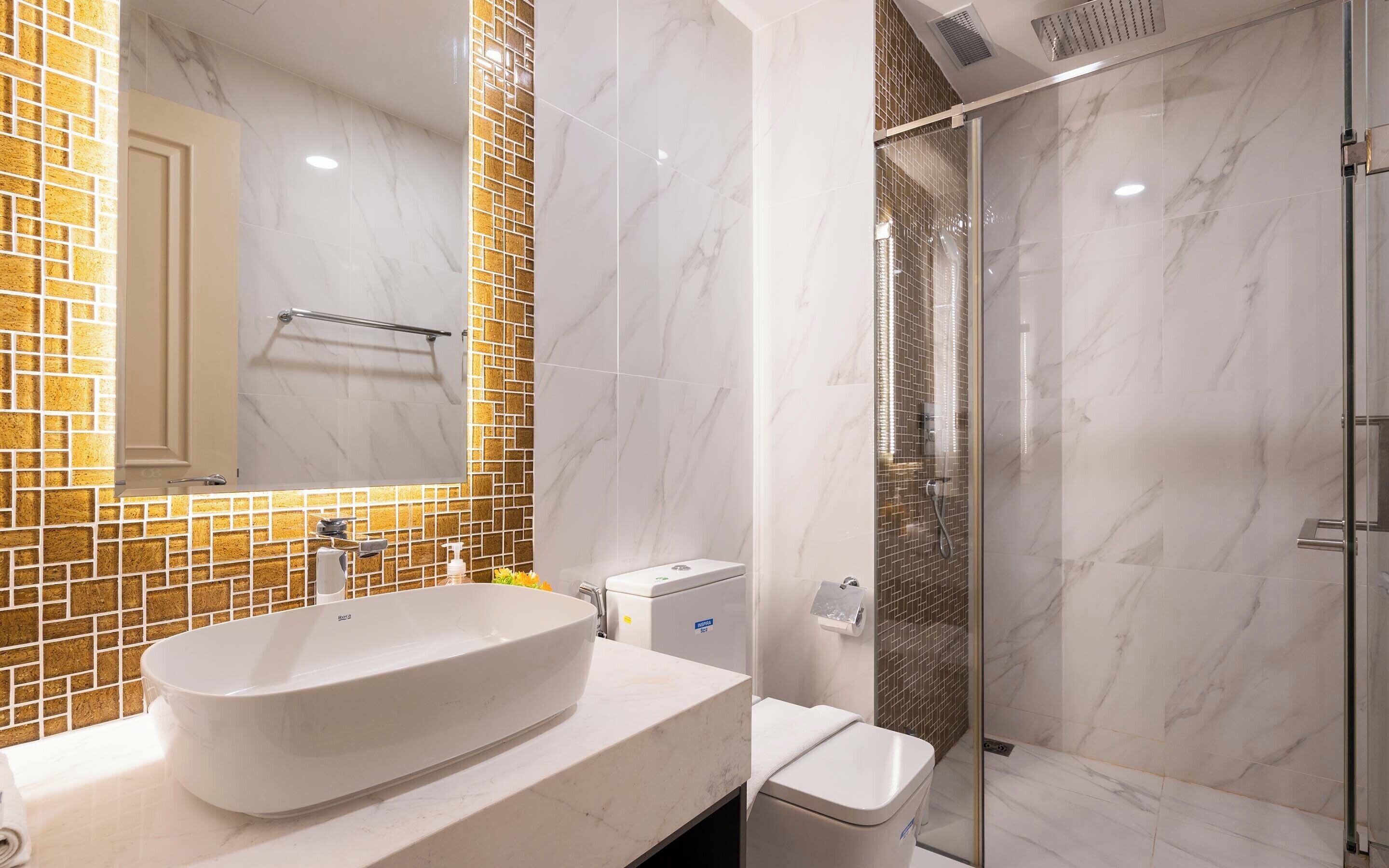 Et badeværelse med en stor hvid vask, en glasvægs brusekabine og et flisebeklædt backsplash.