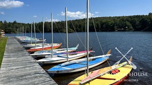A row of colorful sailboats docked at a pier with a forested hill in the background.