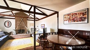A spacious living room with a fireplace, a round wooden table, and a large painting on the wall.