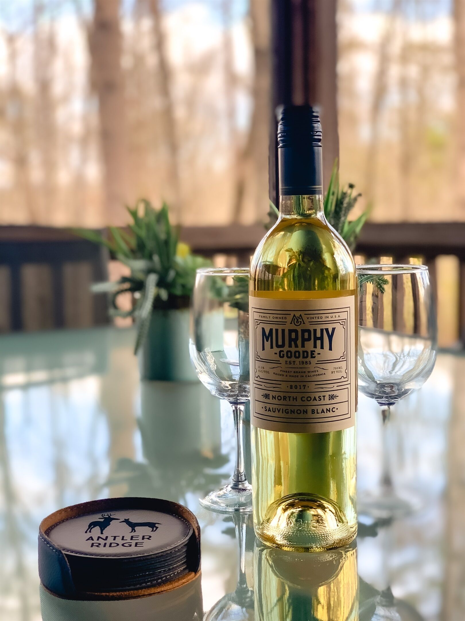 Eine Flasche Murphy Goodee Sauvignon Blanc auf einem Tisch, zusammen mit zwei Gläsern und einem Behälter Antler Ridge Honig.