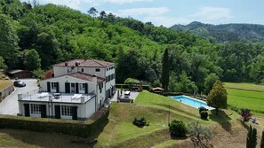A two-story building with a swimming pool, surrounded by lush greenery and hills.