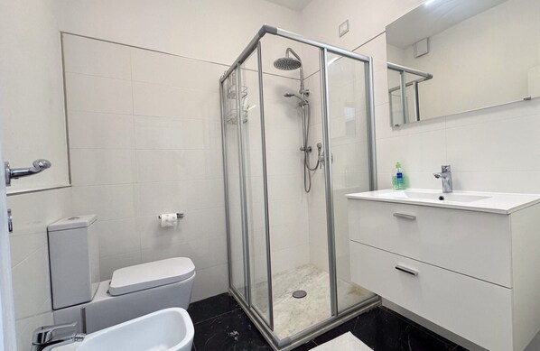A modern bathroom with a glass-enclosed shower, a toilet, a sink, and a mirror.