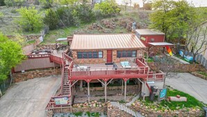 Un edificio de dos plantas con fachada de piedra, techo rojo y un patio cubierto con mesas y sillas al aire libre.