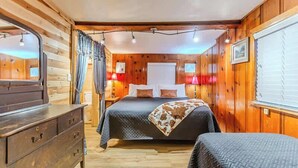 Un dormitorio estilo cabaña acogedor, con interior de madera, una cama con manta estampada, un aparador y una ventana con cortinas.