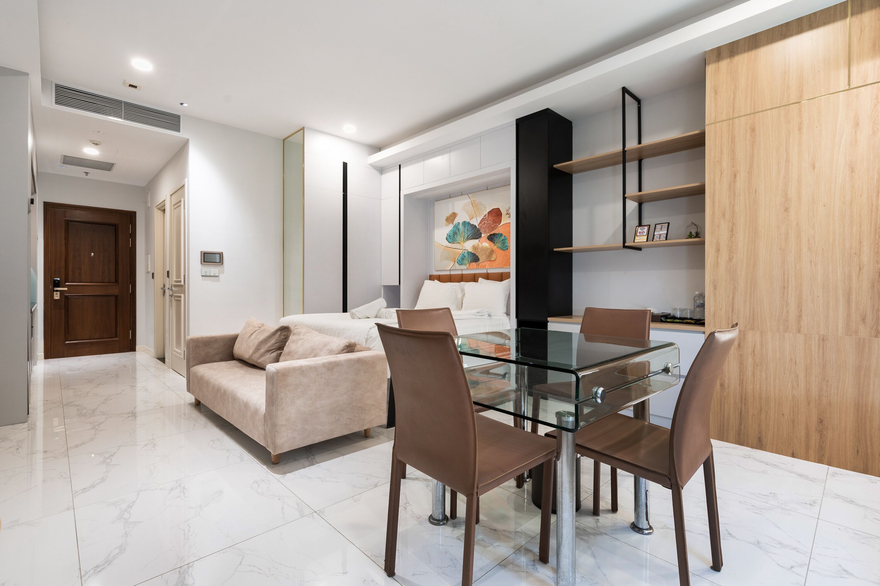 Ein modernes Wohnzimmer mit einem Glastisch, Ledersesseln, einem beigefarbenen Sofa und einem Holzschrank.