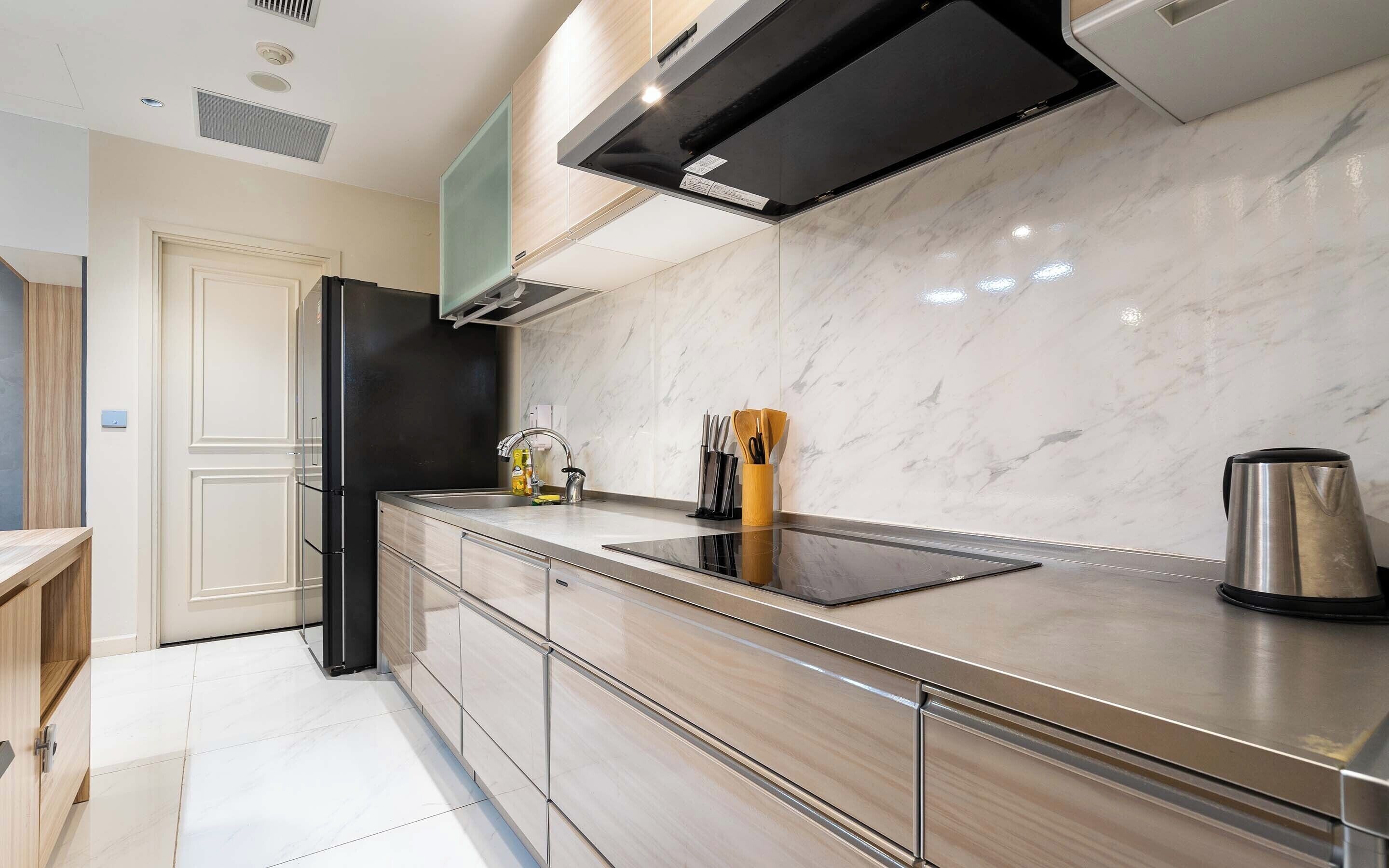 A modern kitchen with a stainless steel countertop, a built-in oven, and a black range hood.