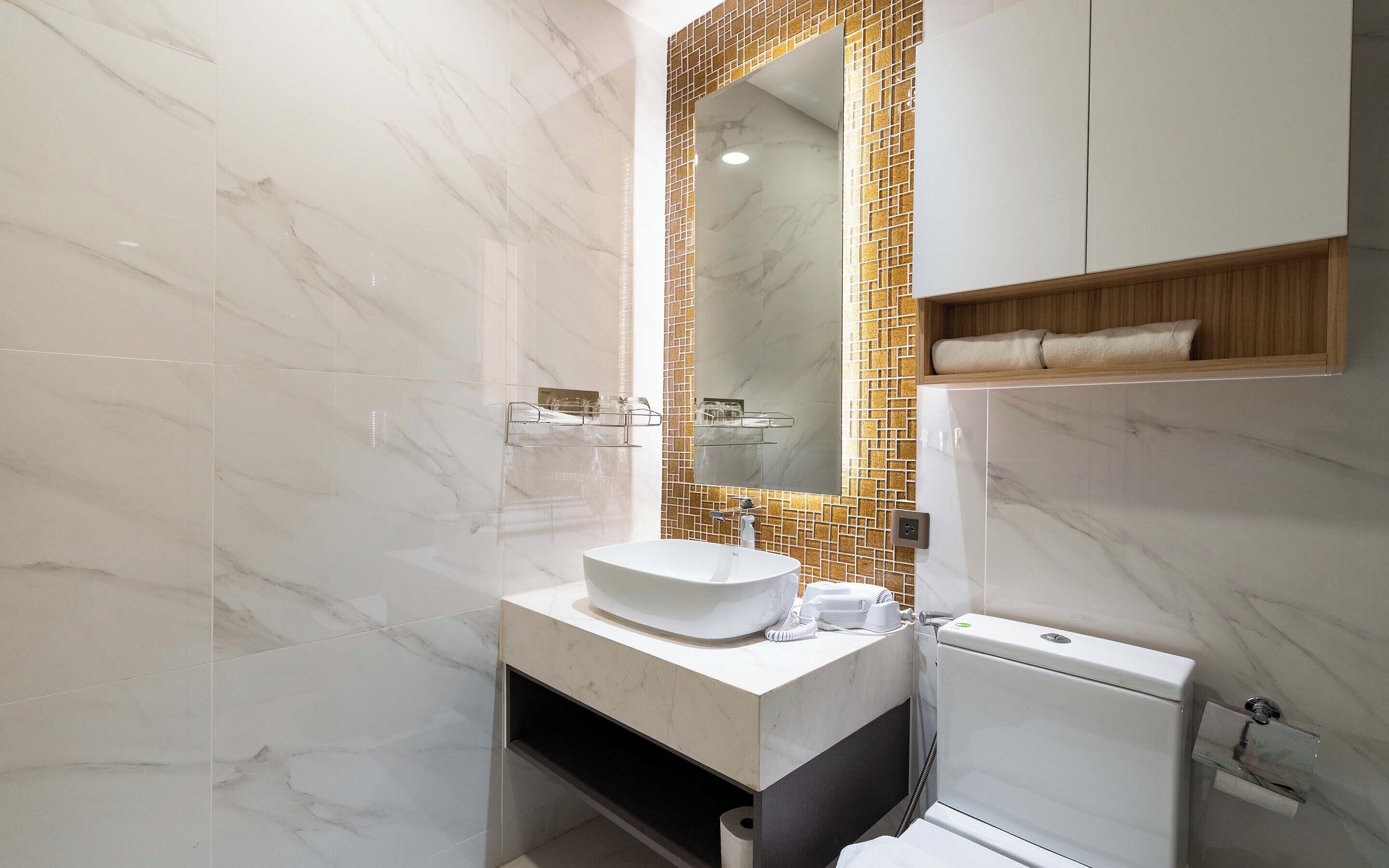 A modern bathroom with a marble vanity, a toilet, and a mirror with a mosaic backsplash.