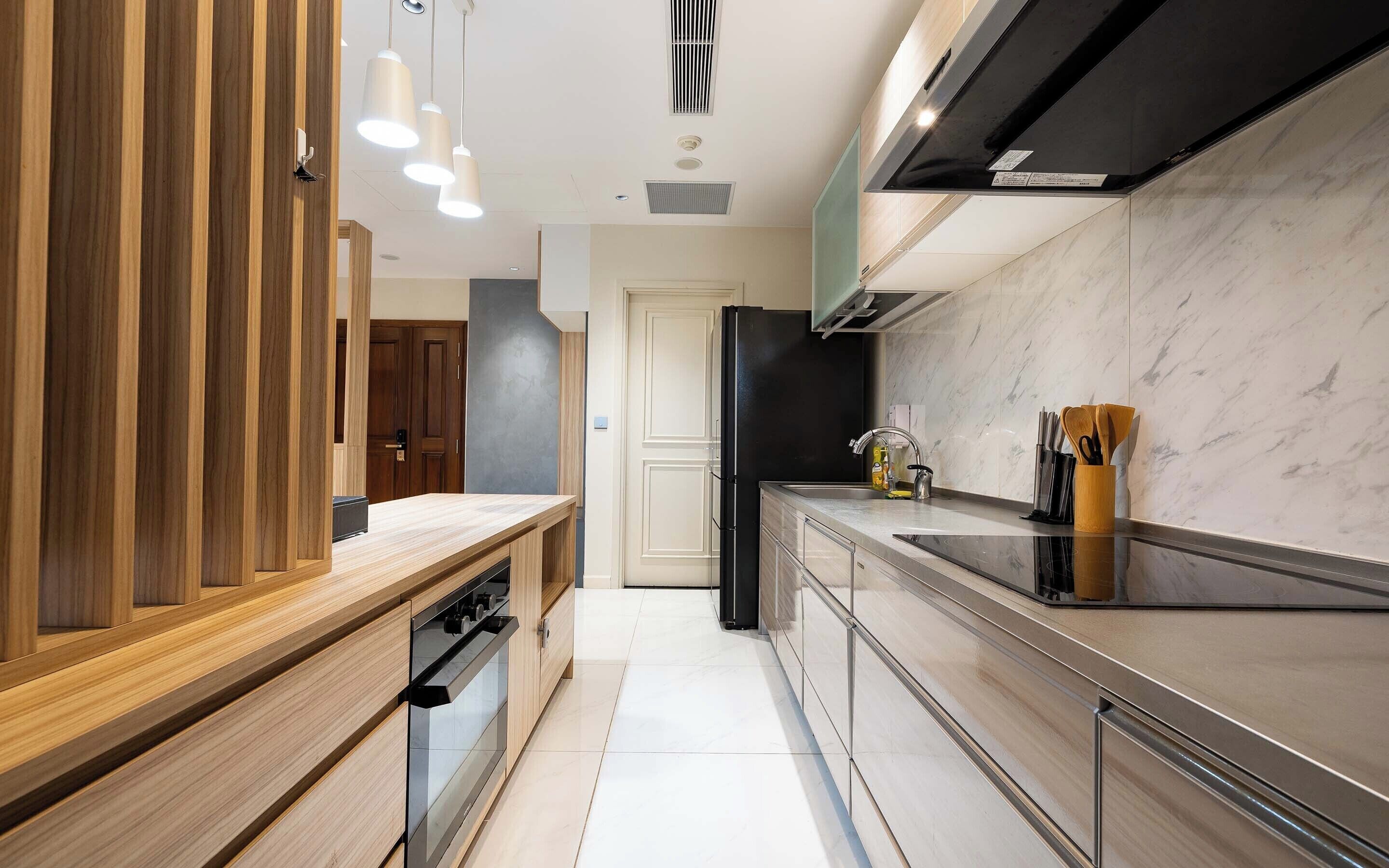A modern kitchen with wooden cabinetry, a stainless steel countertop, and a black refrigerator.