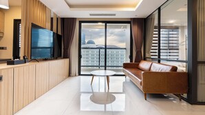 Ein modernes Wohnzimmer mit großem Fernseher, einer Ledersofa, einem kleinen runden Tisch und Blick auf eine Stadtlandschaft durch große Fenster.