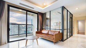 Ein modernes Wohnzimmer mit einer Ledersofa, einem kleinen runden Tisch und einer großen Schiebeglastür, die auf einen Balkon mit Blick auf die Stadt führt.