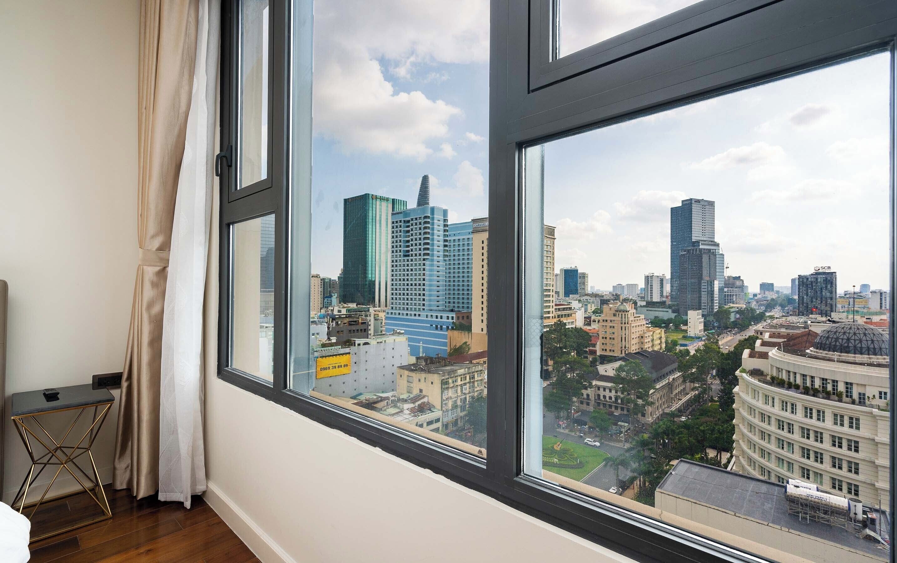 Habitación con un ventanal que ofrece vistas panorámicas de la ciudad, una pequeña mesa y una cortina.