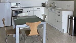 Eine moderne Küche mit weißen Geräten, einem Esstisch mit Stühlen und einer großen Pendelleuchte.