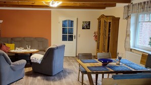 Een gezellige woonkamer met een gebogen bank, twee fauteuils, een klein rond tafeltje en een eettafel met blauwe placemats.