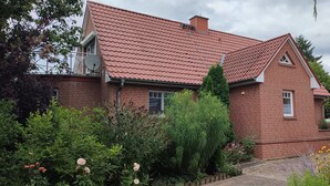 Een bakstenen huis met een rode pannendak, omgeven door diverse planten en bloemen.
