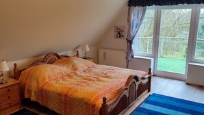 Een slaapkamer met een houten bed, nachtlampjes, een raam met gordijnen en uitzicht op de omgeving.