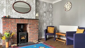 A living room with a brick fireplace, two blue armchairs, a wooden coffee table, and a colorful rug. - Escape to our pet-friendly haven nestled in the heart of Carmarthen. (Carmarthen)