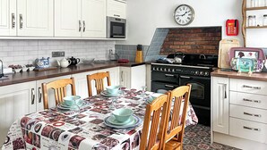 A kitchen with white cabinets, a microwave, a brick wall, a clock, and a table set for dining. - Escape to our pet-friendly haven nestled in the heart of Carmarthen. (Carmarthen)