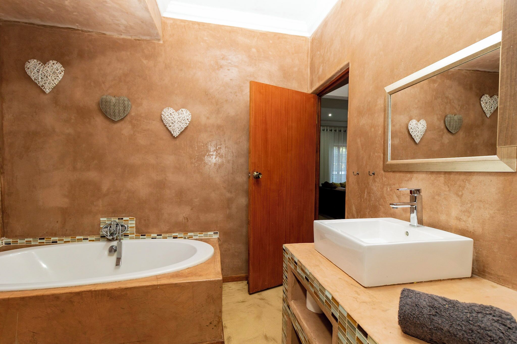 A bathroom with a large bathtub, a sink, and decorative heart-shaped wall art.