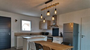 Uma cozinha moderna com uma ilha central, armários de madeira, uma geladeira de aço inoxidável e iluminação pendente.