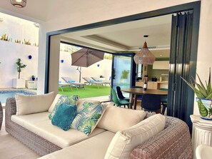 A modern living room with a sofa, a dining table, and a view of a pool and garden. - Moderna Villa con Piscina, a 30 Metros de la Playa, en la Mejor Zona de Marbella (Marbella)