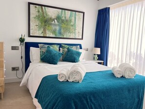 A neatly made bed with a teal bedspread, two blue pillows, and rolled white towels. - Moderna Villa con Piscina, a 30 Metros de la Playa, en la Mejor Zona de Marbella (Marbella)
