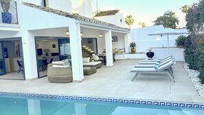 A modern outdoor pool area with lounge chairs, a barbecue grill, and a dining area with a staircase leading to an upper level. - Moderna Villa con Piscina, a 30 Metros de la Playa, en la Mejor Zona de Marbella (Marbella)