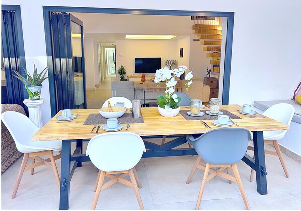 A dining area with a wooden table, white chairs, and a potted plant. - Moderna Villa con Piscina, a 30 Metros de la Playa, en la Mejor Zona de Marbella (Marbella)