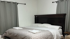 A neatly made bed with a dark headboard, grey curtains, and a tiled floor.