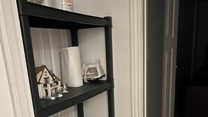 Een zwart metalen schap met diverse spullen, waaronder een modelhuisje, een zakdoos en een bak.