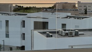 A rooftop with multiple air conditioning units, a view of the sunset over the sea, and a herringbone-patterned floor.