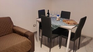 A modern living room with a brown sofa, a dining table set with chairs, a TV mounted on the wall, and a wine bottle. - In the Green of Irpinia locality Montemarano (Avellino) stands Tenuta Casa Arsa. (Casa Arsa)