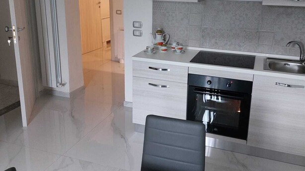 A modern kitchen with white cabinetry, a built-in oven, and a dining area with a black chair. - In the Green of Irpinia locality Montemarano (Avellino) stands Tenuta Casa Arsa. (Casa Arsa)