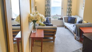 Una sala de estar acogedora con un sofá, una mesa con un jarrón de flores y un espejo grande.