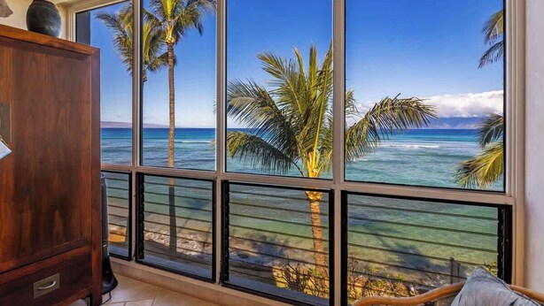 Ein Zimmer mit großen Fenstern und Blick auf das Meer und Palmen.